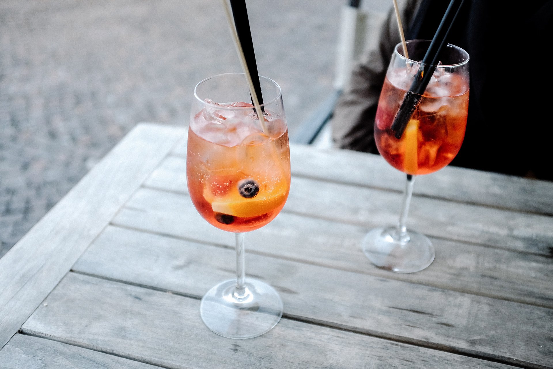 Two glasses of wine with straws on a wooden table.